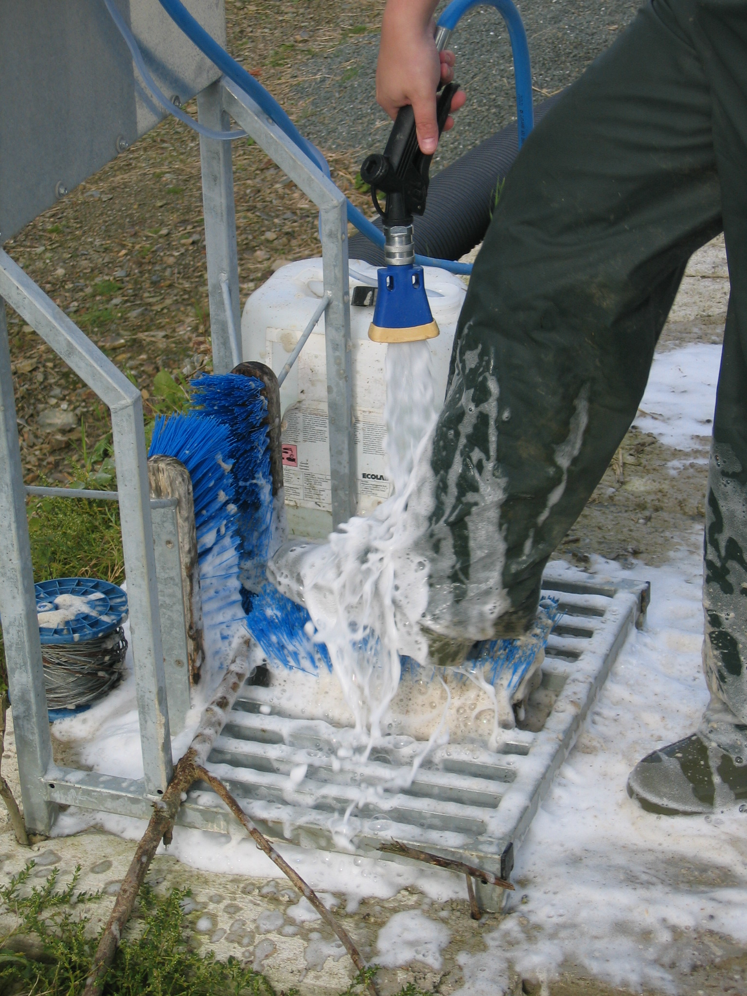 A person using a boot wash containing a spray hose providing disinfectant, brushes and a drain.